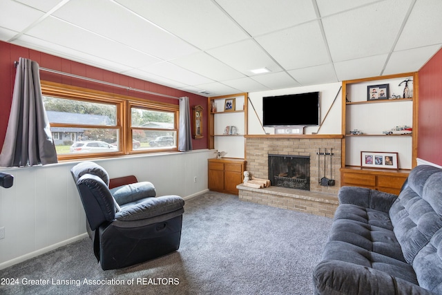 carpeted living room with built in shelves, a fireplace, and a drop ceiling