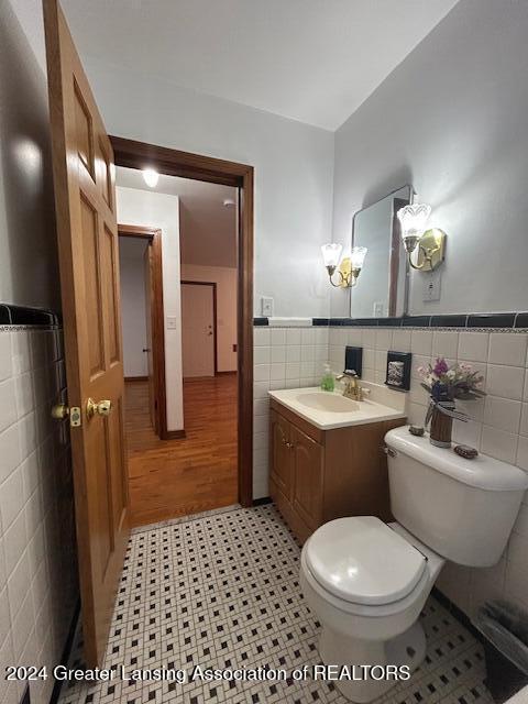 half bathroom featuring a wainscoted wall, vanity, toilet, and tile walls