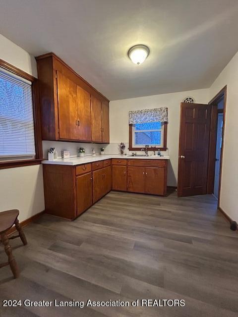 kitchen featuring a sink, baseboards, light countertops, brown cabinetry, and dark wood finished floors