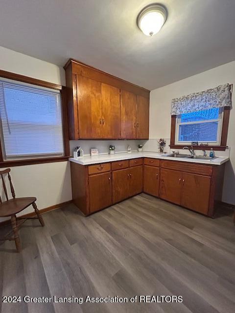 kitchen featuring baseboards, brown cabinets, wood finished floors, light countertops, and a sink