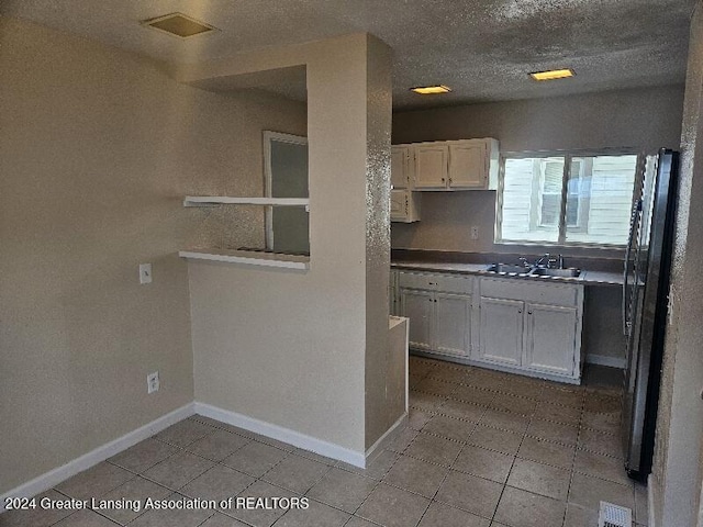 kitchen featuring white cabinetry, sink, and stainless steel refrigerator