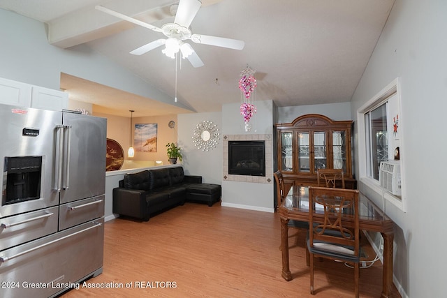 dining space featuring vaulted ceiling with beams, light hardwood / wood-style floors, a tiled fireplace, and ceiling fan