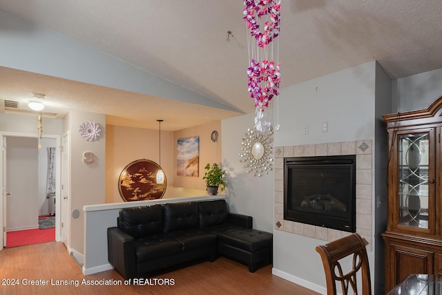 living room featuring vaulted ceiling, a tile fireplace, and light hardwood / wood-style floors