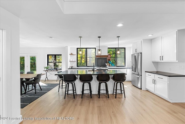 kitchen featuring stainless steel fridge with ice dispenser, white cabinetry, a center island with sink, and light hardwood / wood-style floors