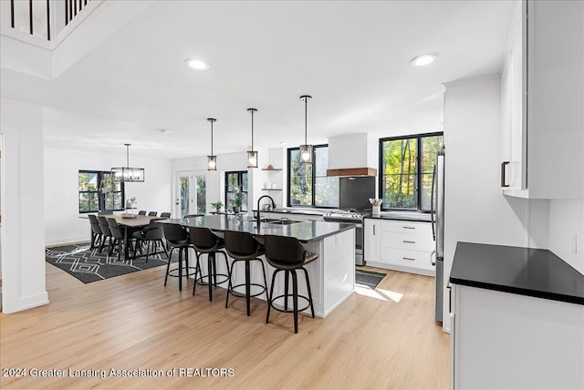 kitchen featuring appliances with stainless steel finishes, white cabinetry, an island with sink, premium range hood, and sink