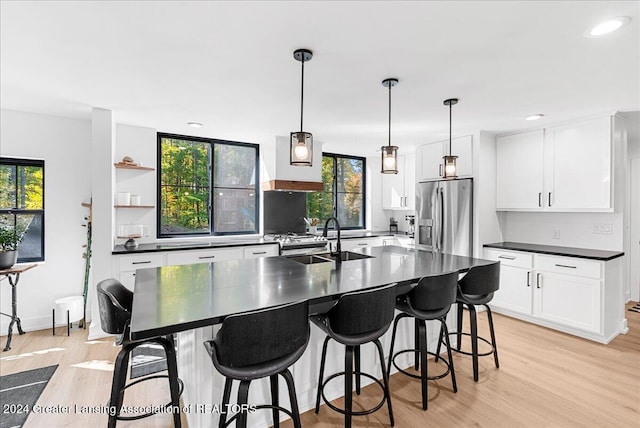 kitchen with stainless steel fridge with ice dispenser, light wood-type flooring, decorative light fixtures, sink, and a center island with sink