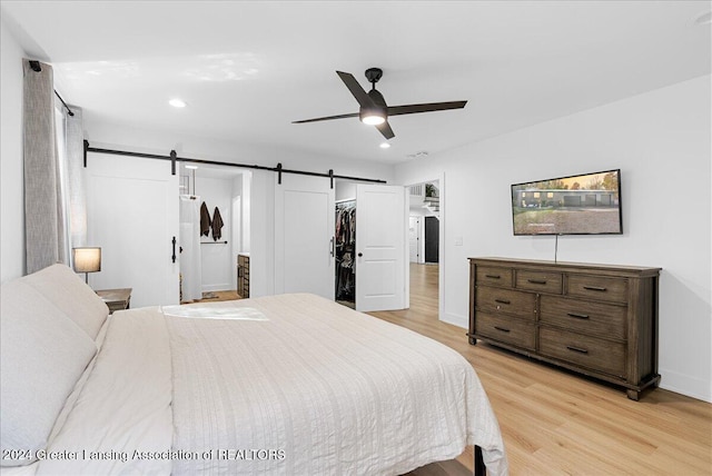 bedroom featuring light hardwood / wood-style flooring, a closet, ceiling fan, and a barn door