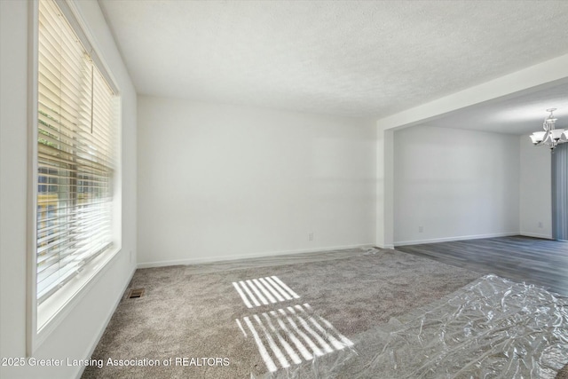 carpeted empty room with a textured ceiling and a notable chandelier