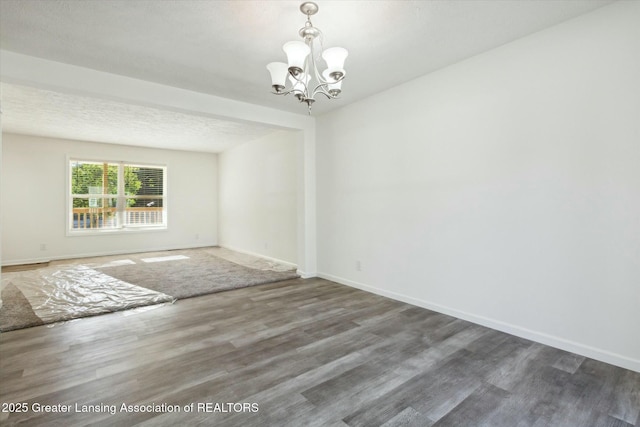 empty room featuring dark wood-type flooring, a textured ceiling, and an inviting chandelier