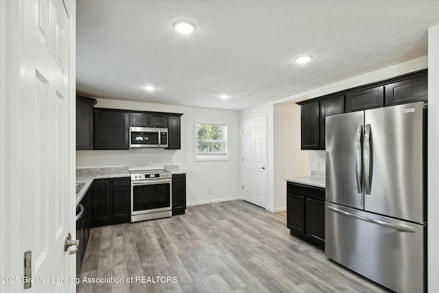 kitchen with light stone counters, light hardwood / wood-style flooring, stainless steel appliances, and a textured ceiling