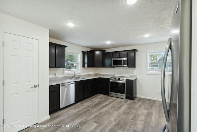 kitchen featuring appliances with stainless steel finishes, sink, light stone countertops, a textured ceiling, and light hardwood / wood-style flooring