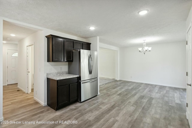 kitchen featuring light hardwood / wood-style flooring, stainless steel fridge, dark brown cabinets, light stone counters, and a textured ceiling