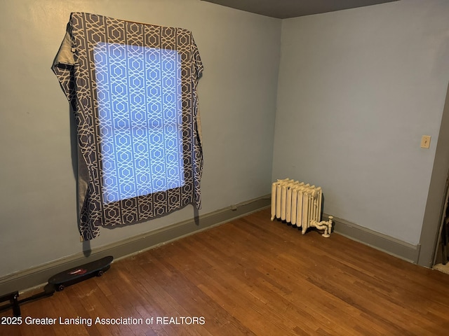 unfurnished room featuring radiator heating unit, baseboards, and wood finished floors