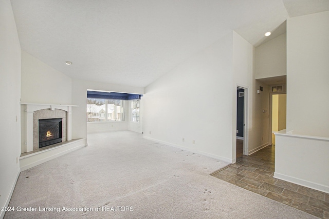 unfurnished living room with a tiled fireplace, carpet floors, and lofted ceiling