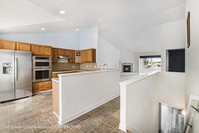 kitchen featuring high vaulted ceiling, appliances with stainless steel finishes, kitchen peninsula, and tasteful backsplash