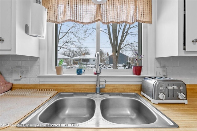 kitchen with tasteful backsplash, white cabinets, sink, and a wealth of natural light