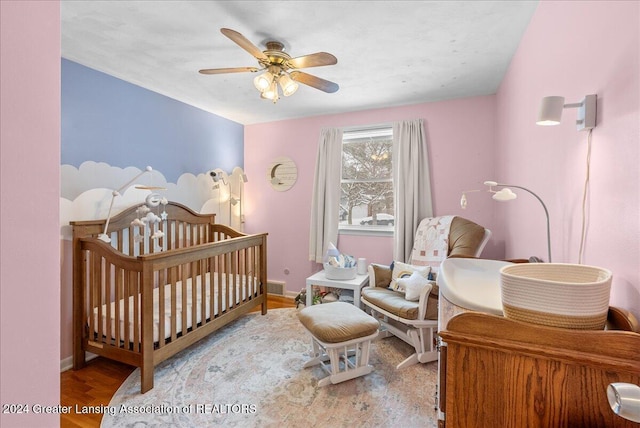 bedroom featuring a nursery area, ceiling fan, and wood-type flooring