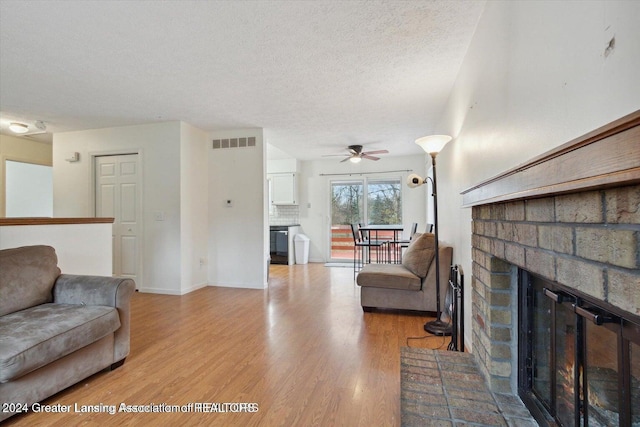 living room featuring a fireplace, light hardwood / wood-style floors, a textured ceiling, and ceiling fan