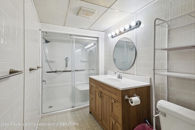 bathroom featuring walk in shower, vanity, toilet, and tile walls