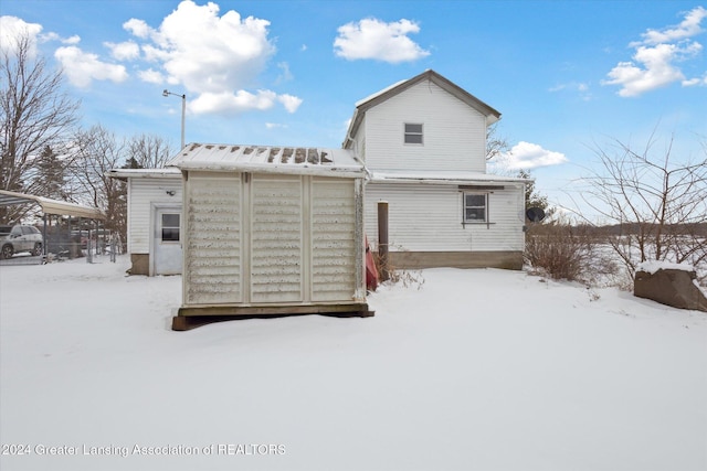 snow covered back of property featuring a storage shed