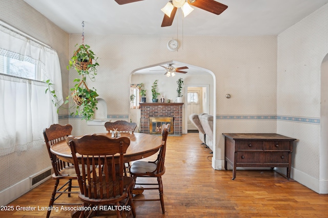 dining space featuring a brick fireplace, wood-type flooring, and ceiling fan