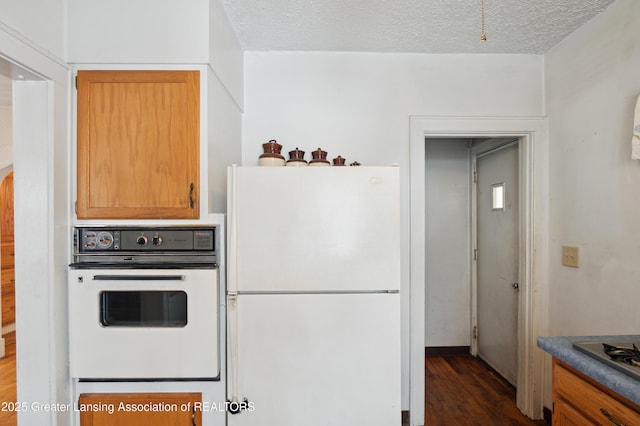 kitchen with dark wood-type flooring, a textured ceiling, and white appliances