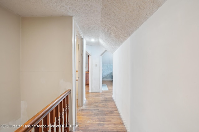 corridor featuring hardwood / wood-style floors, vaulted ceiling, and a textured ceiling