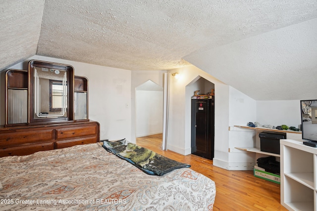 bedroom with lofted ceiling, a textured ceiling, and light wood-type flooring