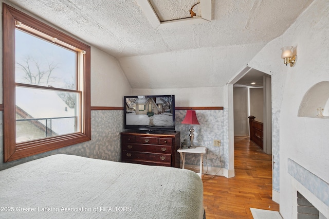 bedroom with wood-type flooring, vaulted ceiling, and a textured ceiling