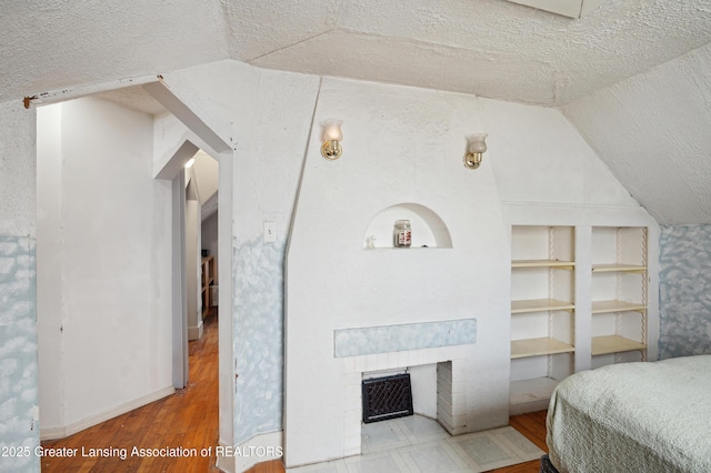 bedroom featuring vaulted ceiling, hardwood / wood-style floors, a fireplace, and a textured ceiling