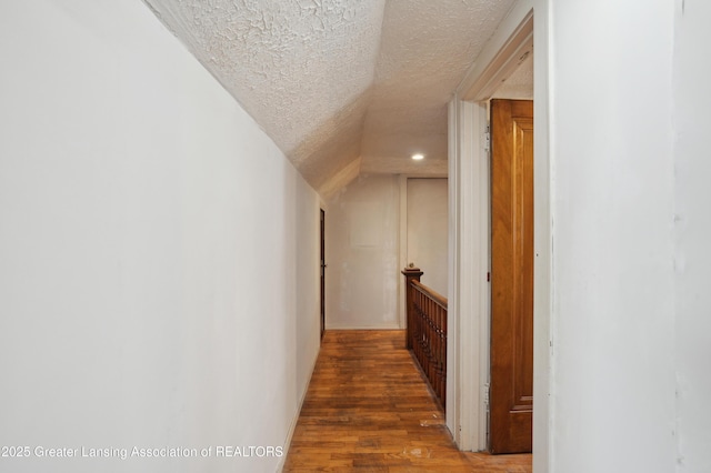 corridor with dark hardwood / wood-style flooring, lofted ceiling, and a textured ceiling