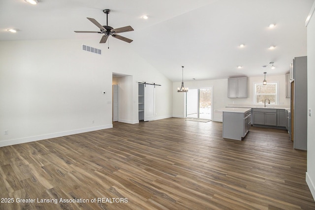 unfurnished living room with a barn door, sink, high vaulted ceiling, ceiling fan with notable chandelier, and dark hardwood / wood-style floors