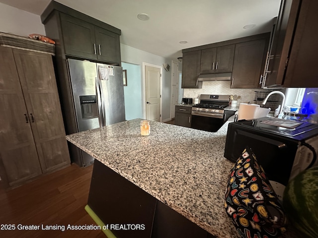 kitchen featuring dark wood-type flooring, dark brown cabinetry, light stone counters, appliances with stainless steel finishes, and decorative backsplash