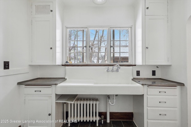 interior space featuring tile patterned flooring, radiator, sink, and white cabinets