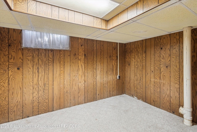 basement featuring carpet, a drop ceiling, and wooden walls