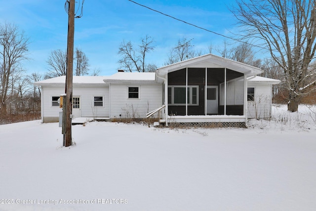 snow covered back of property featuring a sunroom