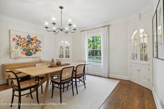 dining space with ornamental molding, a notable chandelier, baseboards, and wood finished floors