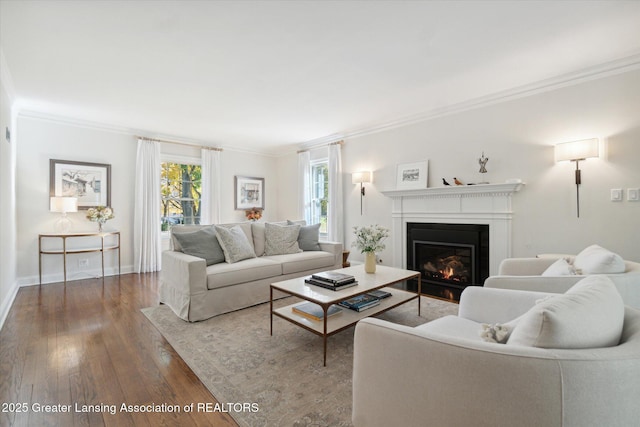 living area featuring a warm lit fireplace, wood-type flooring, baseboards, and crown molding