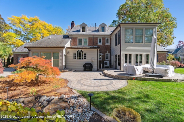 rear view of property featuring brick siding, a lawn, a chimney, and a patio