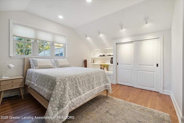 bedroom with baseboards, lofted ceiling, wood finished floors, a closet, and recessed lighting