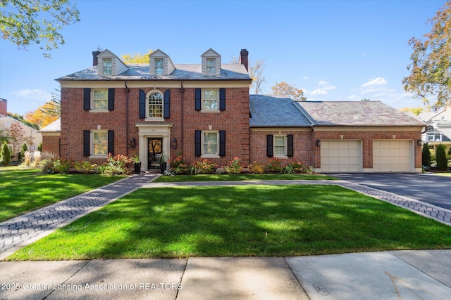 colonial inspired home with a front lawn, brick siding, driveway, and an attached garage