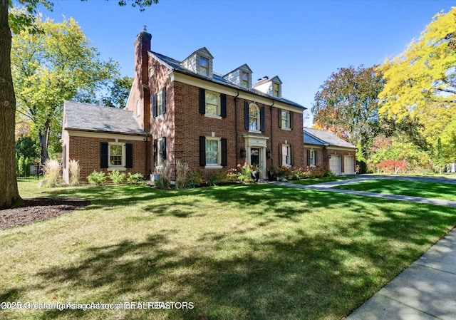 colonial inspired home with brick siding, a chimney, an attached garage, and a front lawn