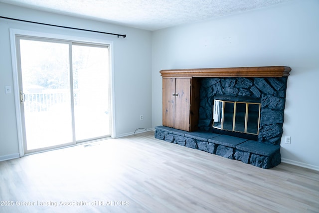 unfurnished living room featuring a stone fireplace, light hardwood / wood-style floors, and a textured ceiling