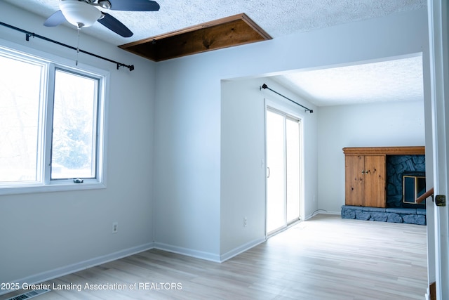 spare room featuring ceiling fan, light hardwood / wood-style floors, a textured ceiling, and a wealth of natural light