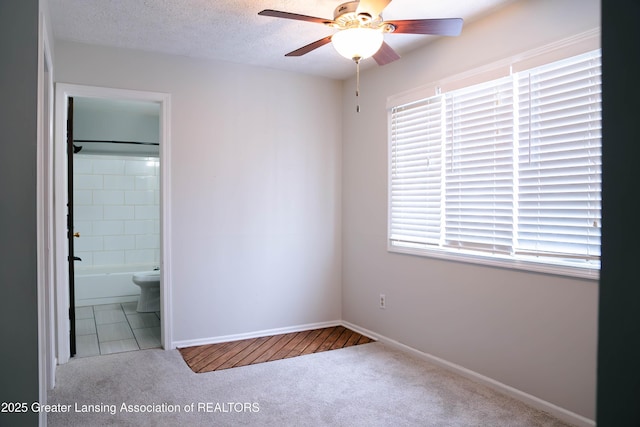 unfurnished bedroom with ceiling fan, connected bathroom, carpet, and a textured ceiling