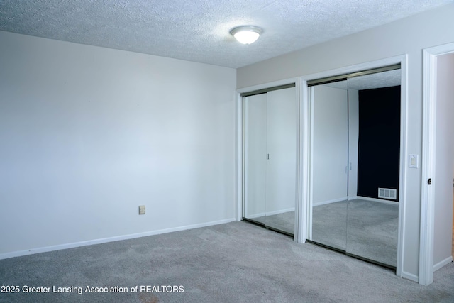 unfurnished bedroom featuring two closets, light colored carpet, and a textured ceiling