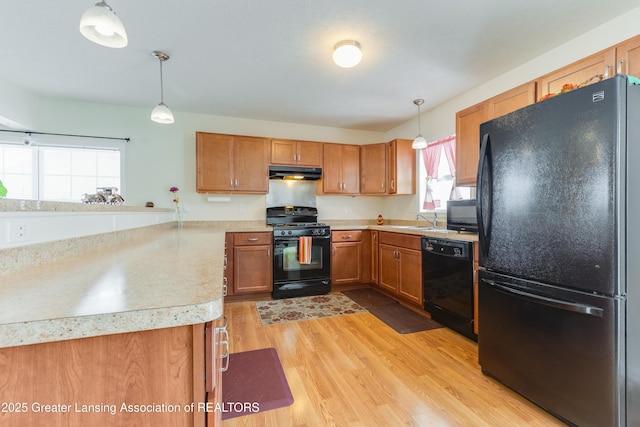 kitchen featuring light wood-style floors, brown cabinets, under cabinet range hood, light countertops, and black appliances