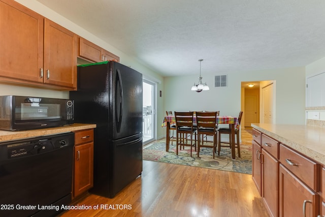 kitchen with light countertops, visible vents, brown cabinetry, light wood-type flooring, and black appliances