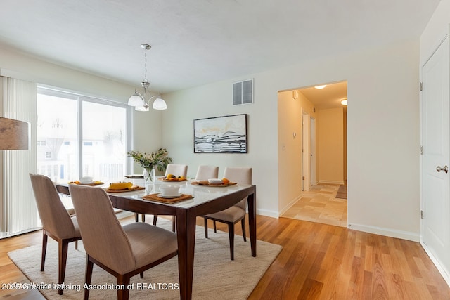 dining space with light wood-type flooring, baseboards, visible vents, and a chandelier