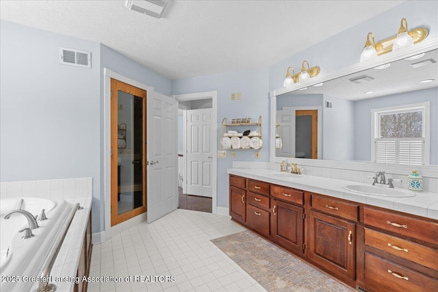 bathroom featuring vanity, tiled tub, tile patterned floors, and a textured ceiling